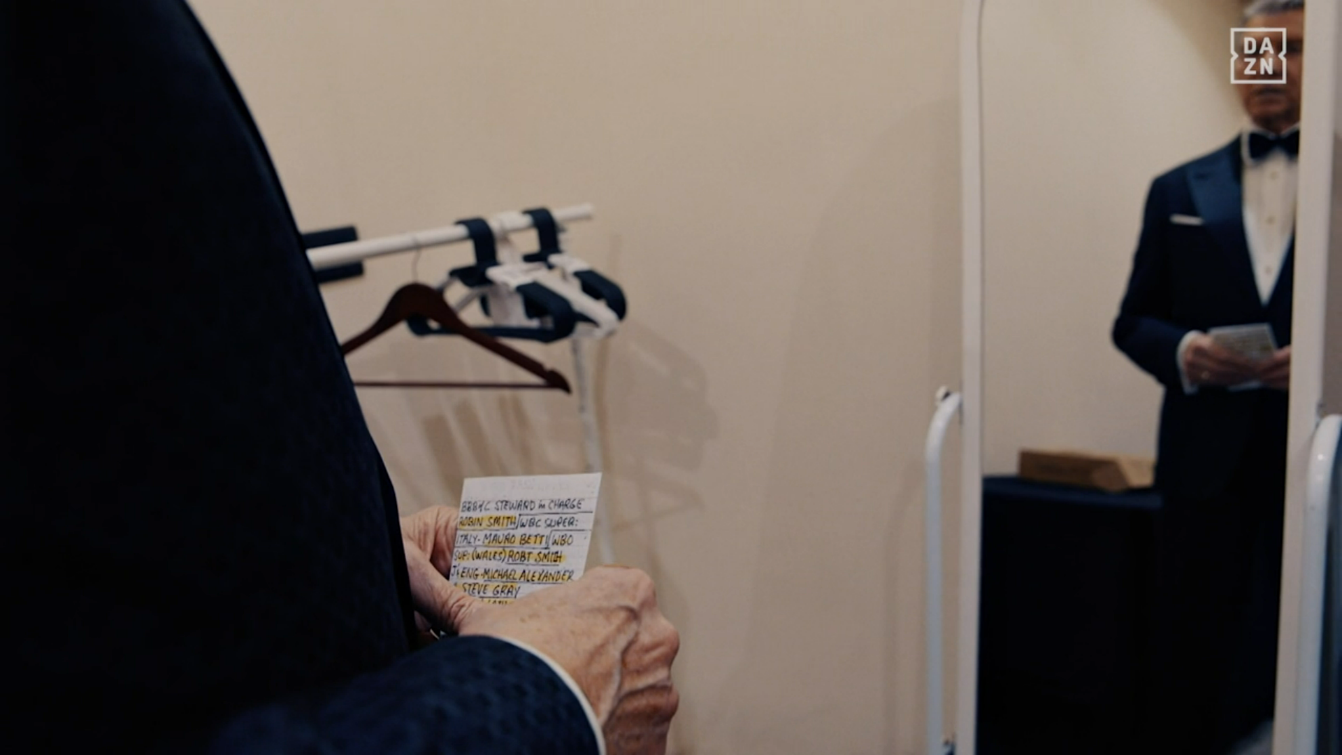 Michael Buffer looking in the mirror in his dressing room, the camera angle shows the names/organisations of all the various supervisors sanctioning the bouts