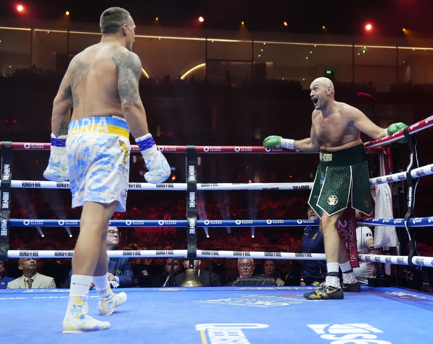 Fury, in the first round, standing in the corner making a silly face for the crowd as his flab folds over itself above his high shorts. Usyk is walking towards him menacingly with his hands down. Their positions in the picture are reminiscent of the Dio walk meme from Jojo's Bizarre Adventure.