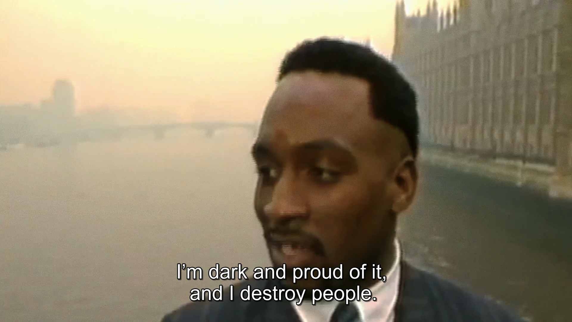 Nigel "The Dark Destroyer" Benn standing on Westminster Bridge with Parliament behind him, he's subtitled as saying "I'm dark and proud of it, and I destroy people."